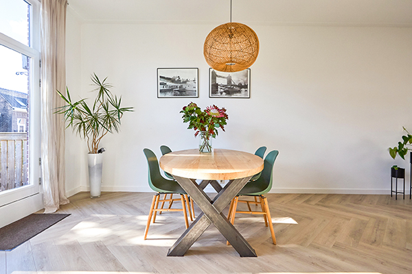 een warme eethoek met stoere poten en een mooie lichte visgraat vloer. de ruimte is licht met mooie bloemen en planten.